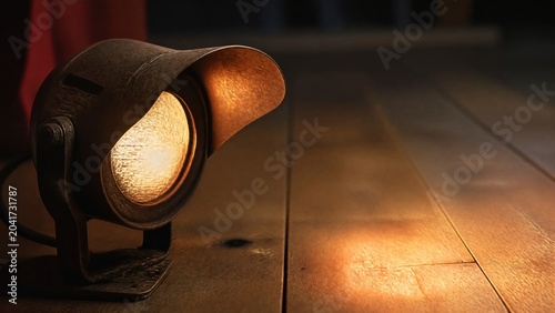  Vintage footlight with warm glow illuminating wood grain of a stage floor. 