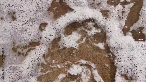 relaxing top down view gentle ocean wave with white foam bubbling and washing over wet brown sand tranquil shoreline, creating soothing and peaceful natural background.