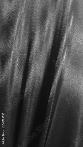 Luxurious black satin fabric flows with elegant folds, creating a sleek and sophisticated texture full of depth and shine.