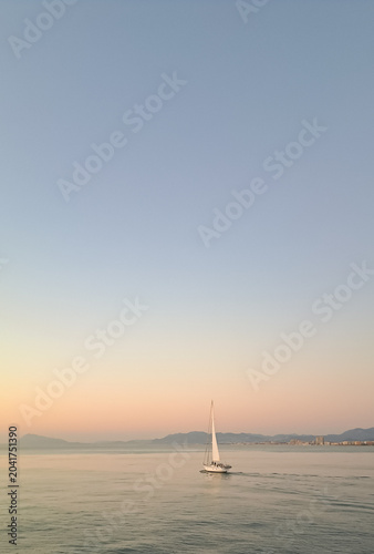Fotografie Minimalist seascape with a white sailboat cruising on calm sea water at sunset, pastel gradient sky background with copy space