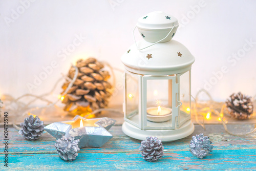 Merry Christmas greeting card template; white lantern with burning candle, pine cones and christmas lights on a old wooden blue paint table against white background
