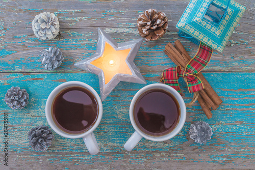 Merry Christmas greeting card template; two cups of coffee or tea, pine cones and christmas lights top view on an old blue paint wooden background