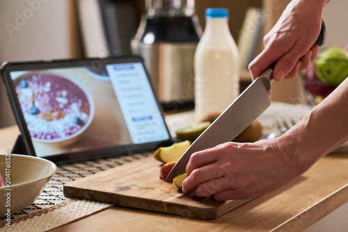Foto Close up of middle aged woman hands cutting fruit on board while following tablet recipe at home, learning cooking skills online