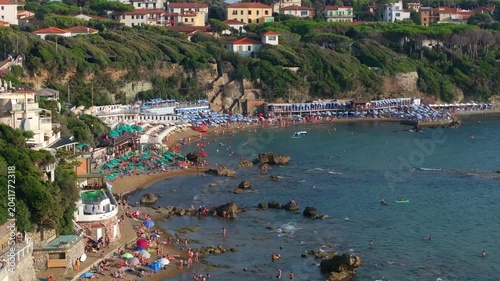 sideways view of the beach scene with waders, swimmers and tourists lining the beach in Castiglioncello, Italy, Tuscan shoreline popular with the jetset