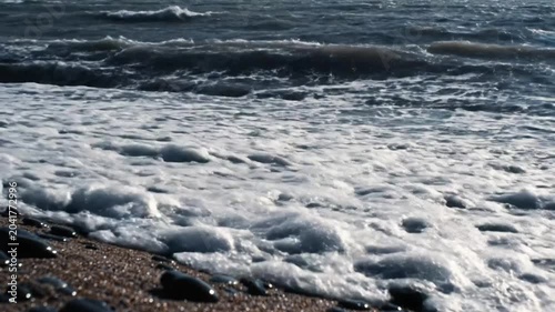 Powerful ocean waves crashing onto a pebbled beach, creating a foamy white water surge during a storm