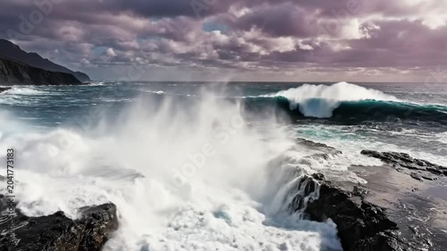 Epic Ocean Waves Crashing Against Rocky Coastline with Dramatic Cloudy Sky during a Stormy Day