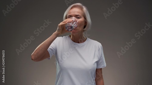 Old woman drinking water, smile mature woman for health, vision or wellness. Beverage, happy pensioner person. Senior female hold glass with aqua for hydration, liquid, fluid and minerals for thirsty