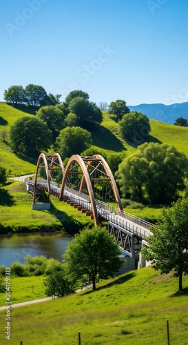 Arched Wooden Bridge Crossing River in Green Rolling Hills Landscape