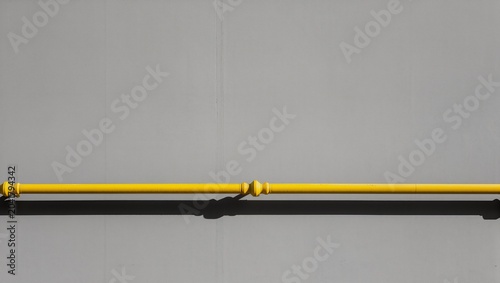 Minimalist Architectural Detail of a Yellow Gas Pipe Running horizontally on a Grey Wall