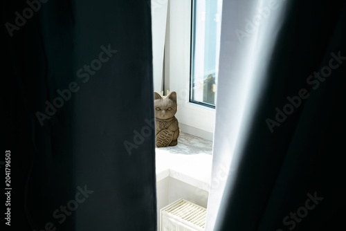 Cardboard lucky cat figurine peeking through dark window curtains