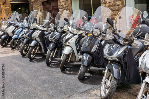 Several motorcycles are marked neatly on a cobbled street in the heart of Florence, surrounded by history medieval buildings and vibrant city life.