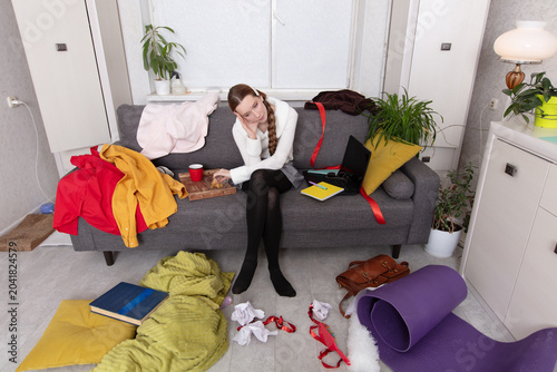 Konstfotografi Messy living room shows a person sitting on a couch surrounded by clutter and di
