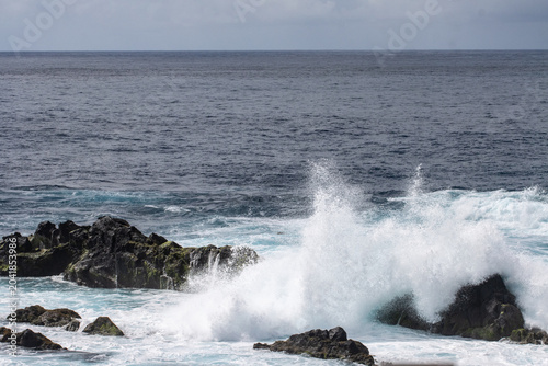 Ocean waves crashing against rocky shoreline under cloudy sky