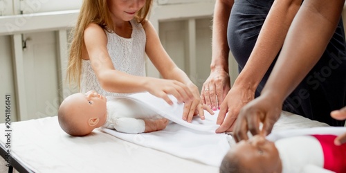 Foto Adults and a child practice swaddling dolls on a table indoors.