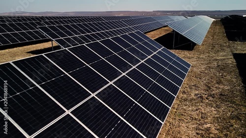 Solar panels arranged in rows on a grassy field under a clear blue sky, showcasing renewable energy technology in a vast outdoor setting