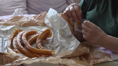 Person dipping a delicious churro into a hot chocolate glass for a typical spanish breakfast, food and cuisine concept
