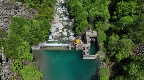 Aerial view of small hydroelectric dam and weir on turquoise mountain river in green Pyrenees forest