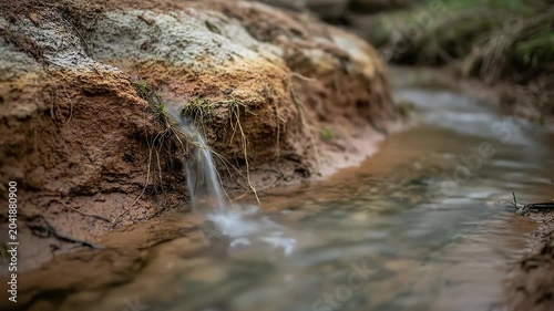 Small Stream Flowing Over a Muddy Clay River Bank