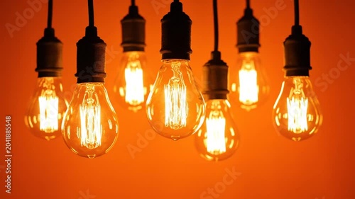 Decorative hanging light bulbs with glowing filaments against a warm orange background