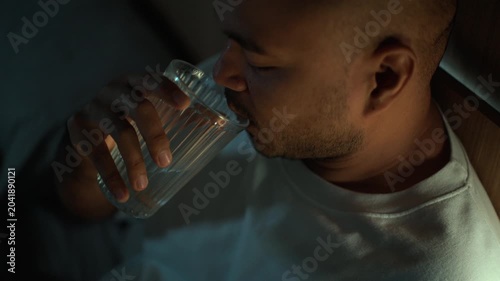 Man taking sleeping pills before bedtime while sitting on bed at home. Sleep aid medication, nighttime routine, stress management, healthcare and wellness concept.
