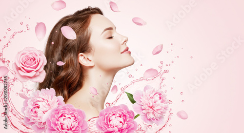 Profile of a young woman with closed eyes surrounded by pink flowers and water splashes. Skincare and beauty concept with roses and peonies. Copy space for text