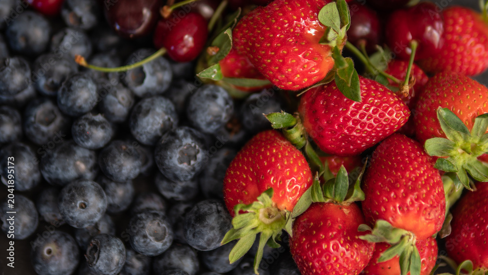 Obraz premium Fresh strawberries and blueberries close up background with ripe summer berries