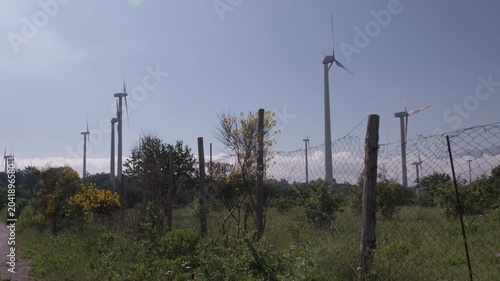 Wind turbines standing in a green field with a fence in the foreground