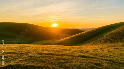 Sunset over rolling green hills with glowing horizon and soft pastel sky