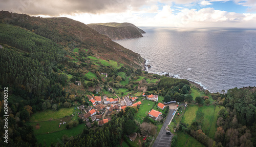 Aerial view of the historic village with white houses nestled among lush green hills and steep cliffs by the Atlantic Ocean Santo Andre de Teixido, A Coruna, Spain.