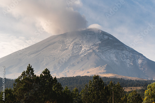 Majestic view of Popocatépetl volcano in Mexico with smoke rising above forested landscape during daytime in autumn perfect for travel and adventure enthusiasts