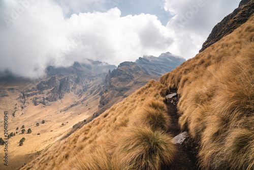 Scenic hiking trail through grassy slopes of Popocatépetl Mexico with dramatic clouds and rugged mountain landscape