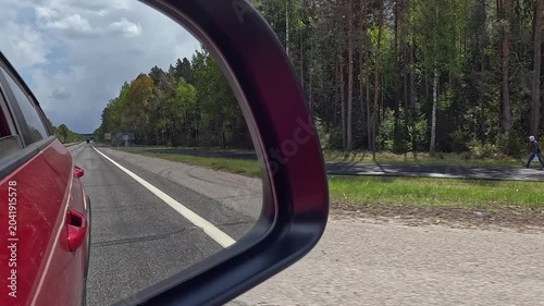View in the rear view side mirror of a automobile, driving a red car along the road