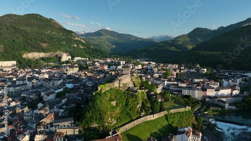Aerial view of Lourdes town and hilltop Chateau fort with river and Pyrenees mountains beyond