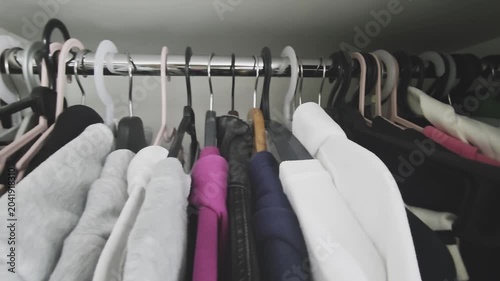 Disorganized wardrobe overflowing with an assortment of vibrant clothing items hanging on a metal rod. A tilted shot slowly zooming out to reveal the chaotic closet