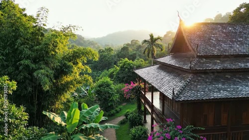 Tranquil view of traditional wooden house with lush green surroundings and mountain landscape during sunrise