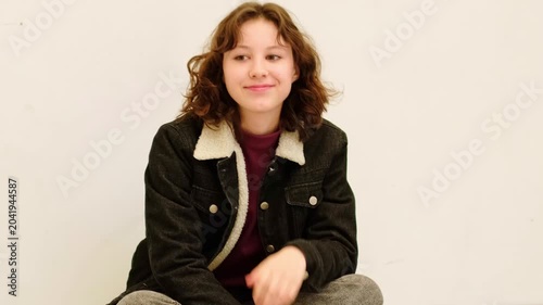 Relaxed teenage girl sitting on the floor with knees up and holding smartphone in both hands, enjoying chatting online after school, concept youth smartphone addiction and everyday screen time.
