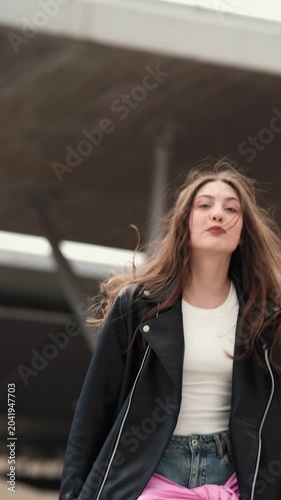 Playful girl with long hair goofs around in a clumsy jumping dance, smiling and moving loosely as if filming a fun social media clip.