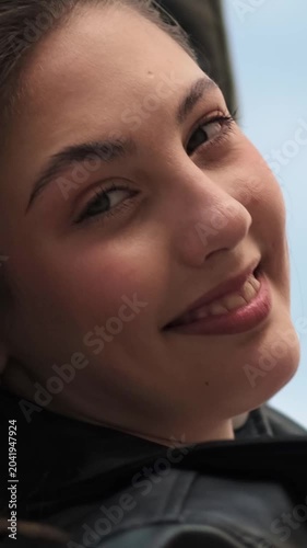 Vertical video of a smiling gen z woman whose face fills the frame while wind plays with her hair, creating a joyful candid social media style shot.
