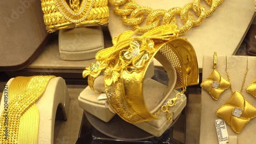 Rotating display of ornate gold jewelry in a shop window featuring wide bracelets, necklace chains, earrings and rings with butterfly and floral designs