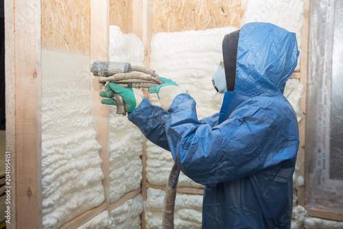 Cuadro en lienzo A construction worker in overalls applies insulation foam to a wooden wall of a