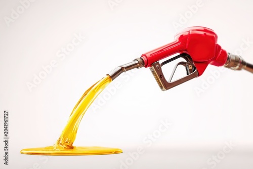 A fuel pump nozzle, against a white background, pouring golden fuel into a puddle. Oil consumption, energy dependence, global oil demand, rising prices, global economic pressures, fuel crisis. Banner