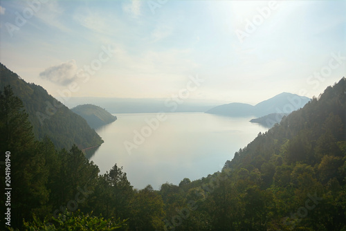 Konstfotografi Misty, and serene view of a large lake surrounded by high, tree-covered mountain