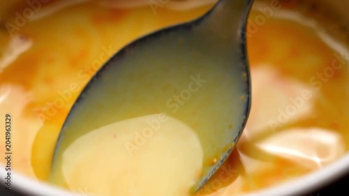 Metal spoon stirring bright orange turmeric powder into warm vegan rice drink to prepare a healing golden milk latte. Traditional ayurvedic wellness concept