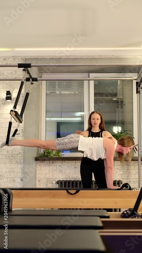 A trainer guides a woman through a demanding Pilates suspension exercise with her body extended above the table. The image highlights client care, strength training, trust, and premium studio service.