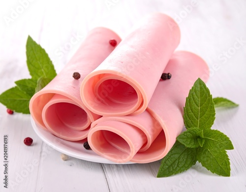 Rolled Pink Deli Meat Slices Arranged on White Plate with Fresh Mint on Wooden Table