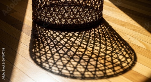 Intricate woven straw sun hat casting complex geometric shadows on a warm wooden floor in bright sunlight