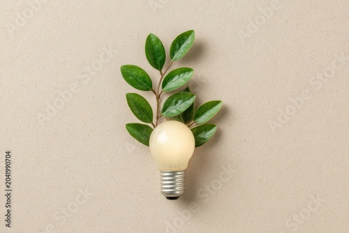 Glow glass bulb and leaves isolated on beige background. Green energy visual. Eco friendly power imagery. Harmony with natural environment. Sustainable energy and renewable sources concept. Eco light