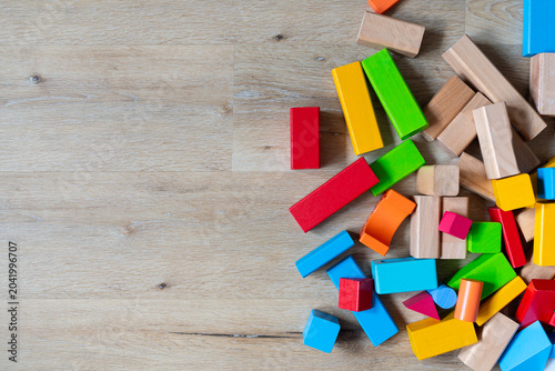top view of colorful wooden toy blocks scattered on a light laminate floor, with large empty copy space on the left side for text