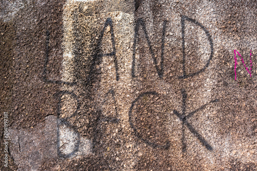 Konstfotografi “Land Back” written in black paint on a textured concrete wall.