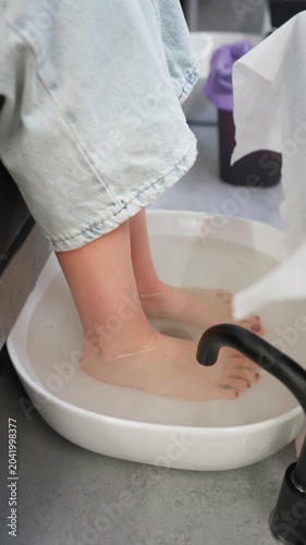 Woman soaking feet in spa bath before pedicure treatment in beauty salon. Concept of foot care, relaxation and wellness. Vertical video